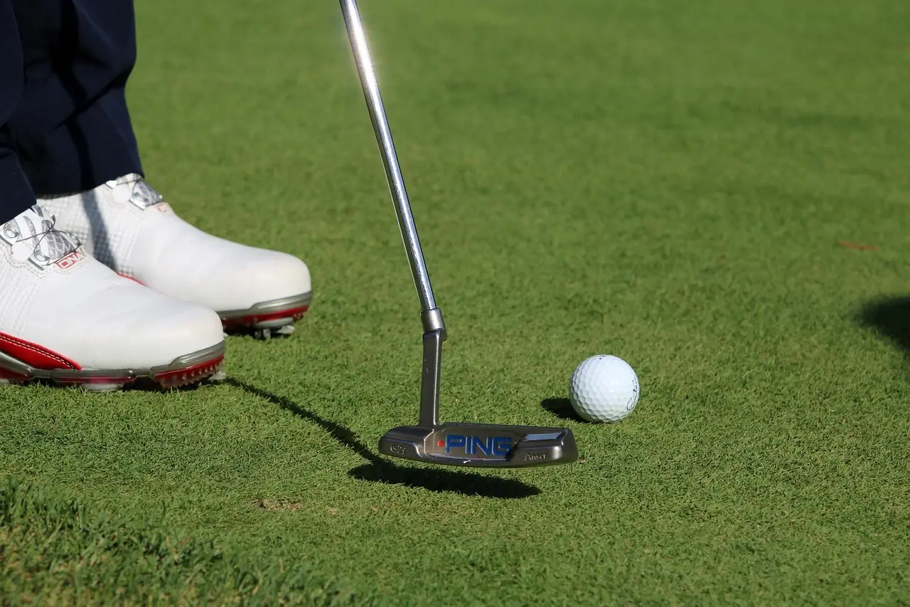 Putter, golfbold og golfsko på green